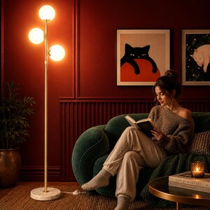 May include: A tall floor lamp with a slender gold-toned metal pole, a circular white marble base, and three spherical white glass shades arranged vertically. The lamp emits a warm, glowing light from each of the three globes.