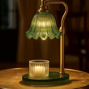Może przedstawiać: Zielona szklana lampa stołowa z falistym kloszem i mosiężnymi akcentami. Lampa ma pasującą zieloną podstawę i mały świecznik. Lampa stoi na okrągłym stole.
