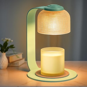 May include: A modern candle warmer lamp in shades of green and yellow. The lamp features a dome-shaped, textured glass shade and a cylindrical candle holder. The base is a circular design with a brown accent.