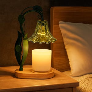 May include: A decorative lamp with a floral design. The lamp features a green metal stem with leaves, a yellow glass shade, and a white candle. The lamp sits on a wooden base, creating a warm, inviting ambiance. The lamp is on a wooden nightstand.