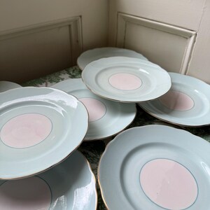 May include: A collection of round ceramic plates featuring a pale mint green border and a solid light pink center circle. Each plate has a scalloped edge and a thin gold-colored rim, creating a consistent design across the set of stacked dinnerware.