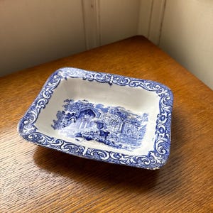 May include: A small, white ceramic dish with a blue and white floral pattern. The dish has a rectangular shape and a slightly raised rim.