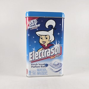 May include: A rectangular blue metal container of Electrasol 3-in-1 Tabs. The container features a cartoon image of a woman with white hair and a red collar. The container has the words "Jet Dry PowerBall" and "Fresh Scent" on it.