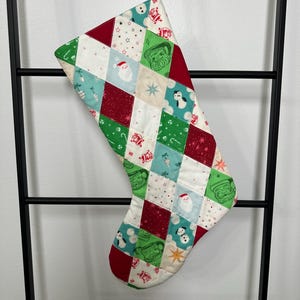 May include: A red and green patchwork Christmas stocking with a variety of holiday-themed designs, including Santa Claus, penguins, snowmen, and stars.