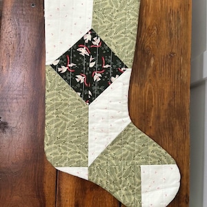 May include: A green, white, and black Christmas stocking with a geometric pattern. The stocking has a white cuff and a green loop at the top.