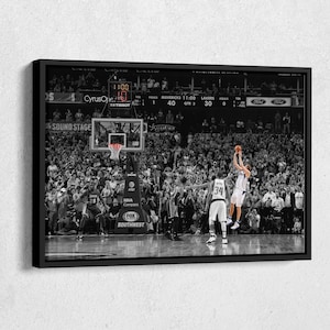 May include: A black and white photo of a basketball player in mid-air, shooting a basketball. The player is wearing a white jersey with the number 34 on it. The player is surrounded by a crowd of people. The scoreboard in the background shows the score as Mavericks 40 and Lakers 30. The clock shows 11:00. The text "Cyrus One" and "SOUND STAGE" are visible on the scoreboard.