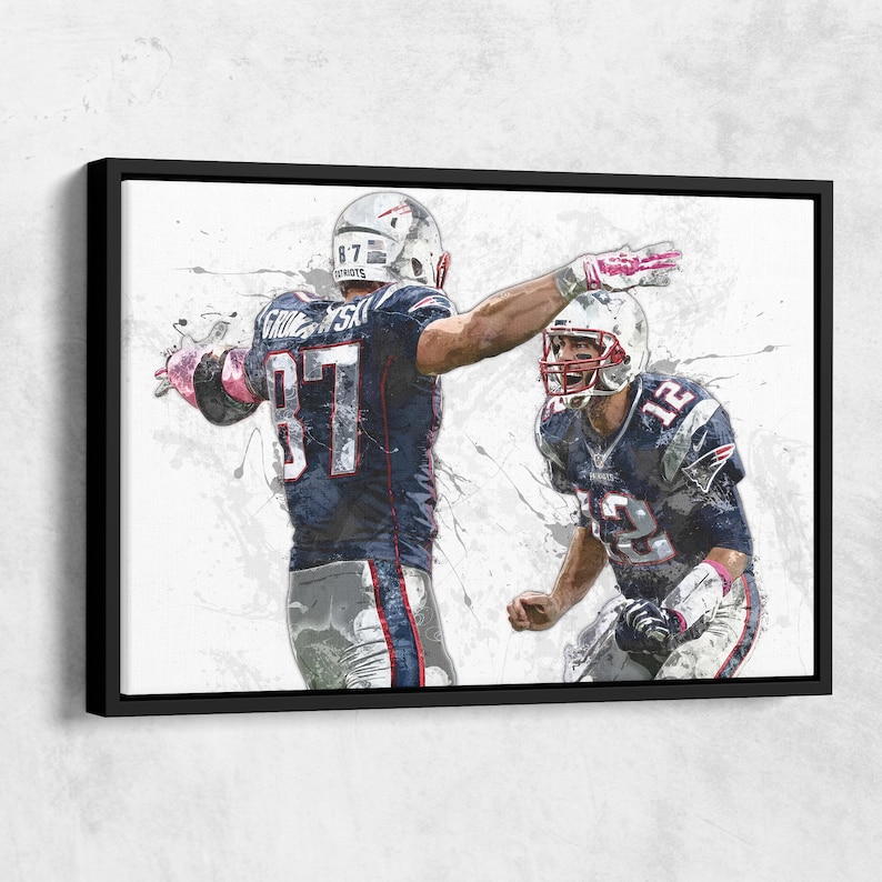K&ouml;nnte beinhalten: Gerahmter Leinwanddruck mit einer stilisierten Illustration von zwei American-Football-Spielern in marineblauen und wei&szlig;en Uniformen. Ein Spieler mit der Nummer 87 hat den Arm erhoben. Der andere Spieler tr&auml;gt die Nummer 12. Der Hintergrund hat wei&szlig;e Farbspritzer.
