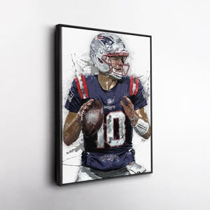 May include: Framed artwork of a football player in a navy blue jersey with the number 10. The player is wearing a silver helmet and holding a football. The artwork has a watercolor effect with white paint splatters.