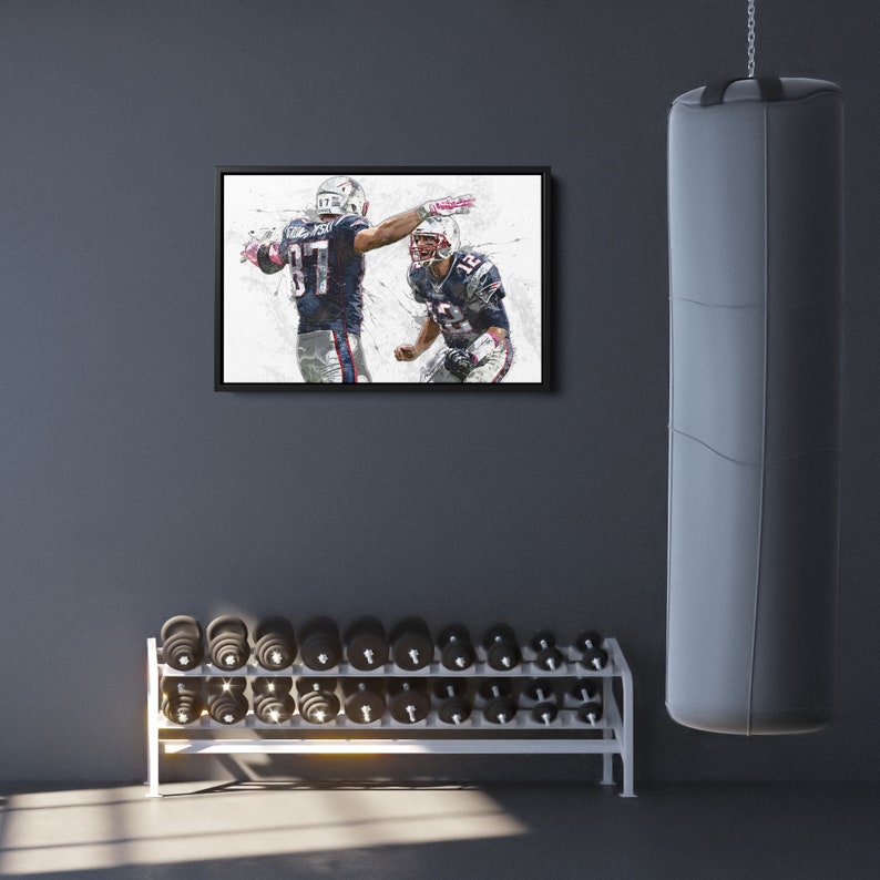 K&ouml;nnte beinhalten: Gerahmtes Kunstwerk mit zwei Footballspielern in marineblauen und wei&szlig;en Uniformen, die ein Spiel feiern. Das Bild im Malstil befindet sich vor einer grauen Wand in einem Fitnessstudio, mit Hantelst&auml;nder und Boxsack.
