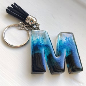 Llavero de resina con letra personalizada, hecho a mano, con borla de ante negro y llavero plateado, estilo volcán de llama azul.