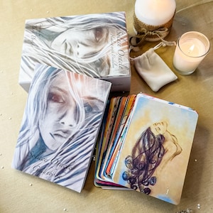 May include: A set of oracle cards with a guidebook and a white crystal pendulum. The cards feature watercolor illustrations of women with flowing hair. The guidebook has the title "Solace Oracle Guidebook" printed on the cover. The box for the cards has the title "Solace Oracle" printed on the cover.