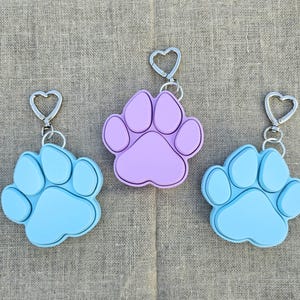 May include: Three paw print keyrings, one light blue, one lavender, and one dark blue. Each keyring has a silver heart-shaped ring.