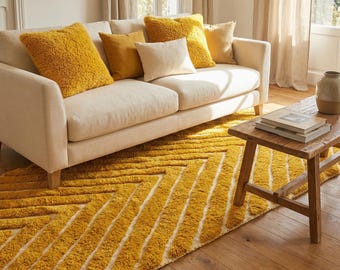 May include: A living room scene featuring a cream-colored sofa adorned with yellow throw pillows. A textured yellow rug with a geometric pattern lies on the wooden floor. A small wooden table and a vase are also present.