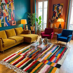 Peut inclure: Un salon coloré avec un canapé d'angle jaune moutarde, un tapis multicolore et deux fauteuils. Le tapis présente des rayures rouges, jaunes, vertes et bleues. Des œuvres d'art ornent les murs et des plantes ajoutent une touche naturelle.