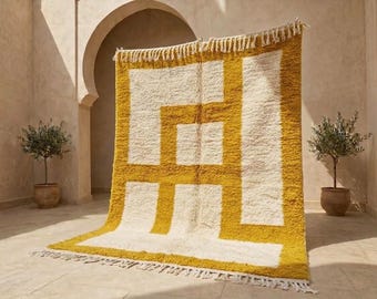 May include: A rectangular area rug featuring a high-pile texture with a bold geometric pattern in mustard yellow and cream white. The design consists of thick, intersecting lines forming rectangular shapes, finished with cream-coloured fringe at both ends.