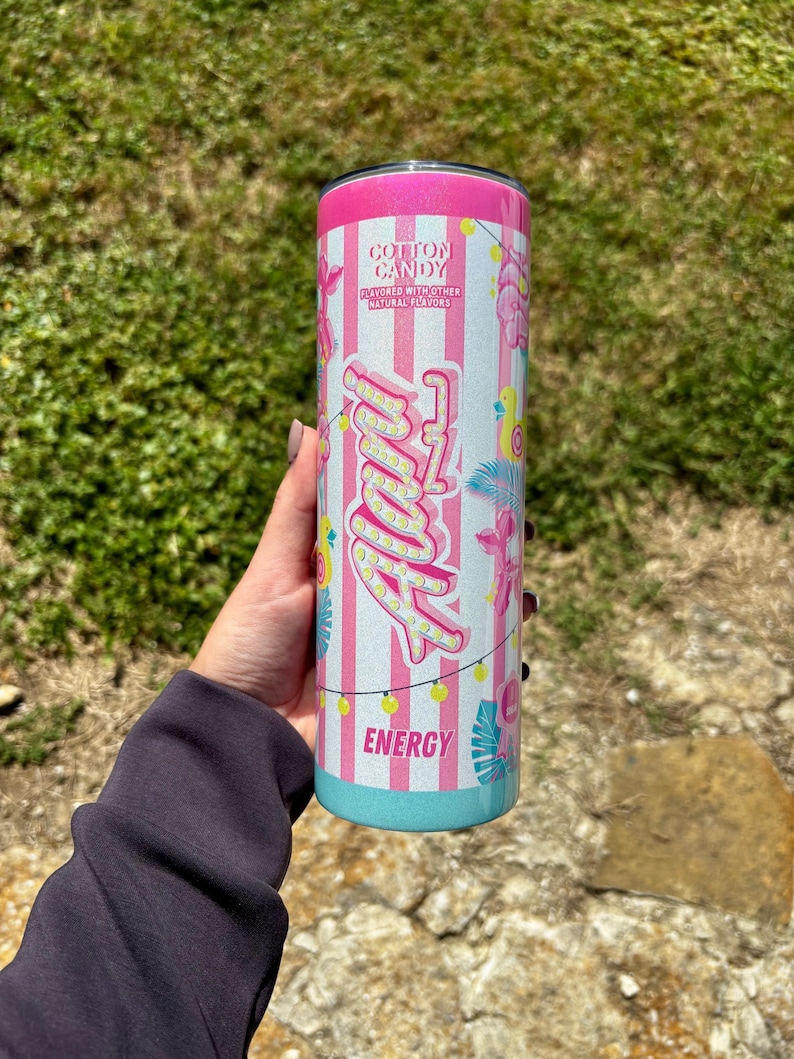 K&ouml;nnte beinhalten: Ein rosa-wei&szlig; gestreifter Becher mit dem Wort "Angel" in einer Schriftart im Leuchtstil. Der Becher hat einen rosa Deckel und einen t&uuml;rkisfarbenen Boden. Der Text "Cotton Candy" und "Energy" sind ebenfalls sichtbar.