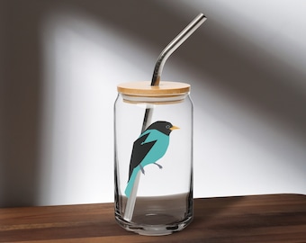 May include: A clear glass tumbler with a bamboo lid and a stainless steel straw. The tumbler features a teal and black bird illustration. The glass sits on a dark wooden surface.