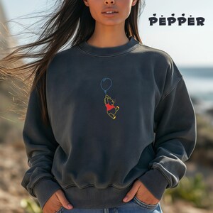 May include: A dark gray sweatshirt with a Winnie the Pooh graphic. Pooh is holding a blue balloon and is flying in the air. The sweatshirt has a crew neck and long sleeves.
