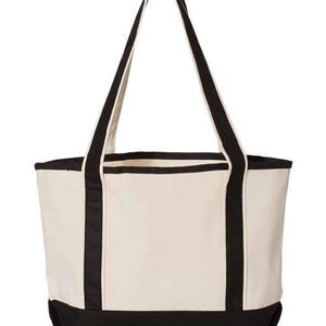 May include: A cream-coloured canvas tote bag with black detailing. The bag has black handles and a black base. The tote bag is designed for carrying items and has a simple, classic style.