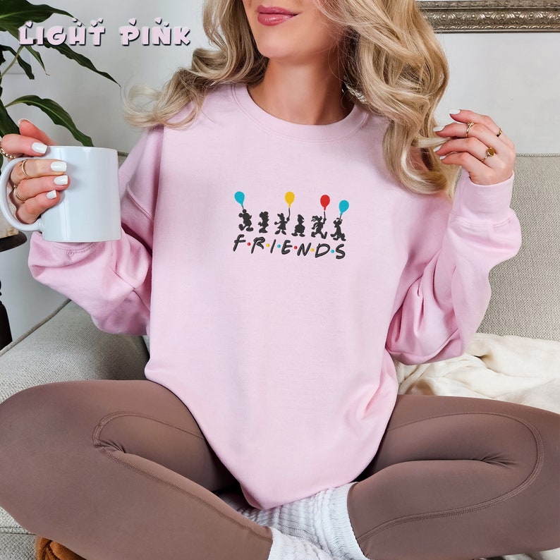 May include: A light pink sweatshirt with a graphic of six figures holding balloons and the text "FRIENDS" underneath.