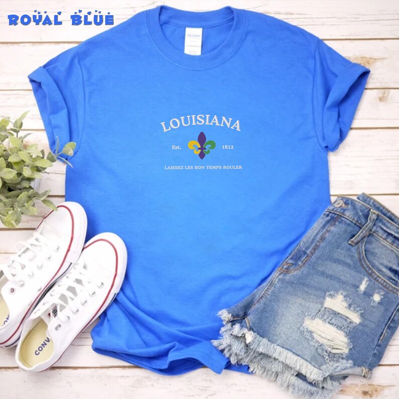 May include: A royal blue t-shirt with a white graphic design that says "Louisiana" with a fleur-de-lis and the text "Est. 1812 Laissez Les Bon Temps Rouler".