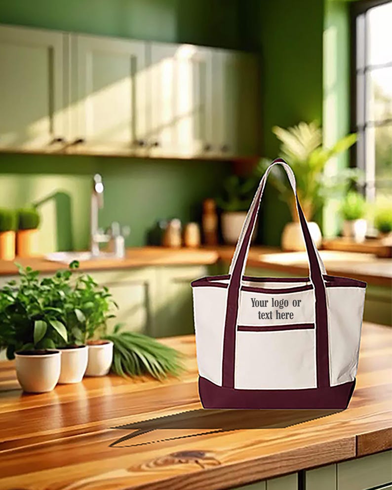 May include: A white tote bag with claret-coloured accents, including the base and handles. The bag features a pocket with the text "Your logo or text here". The bag is on a wooden surface.