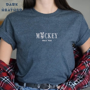 May include: A dark heather grey t-shirt with a white graphic of Mickey Mouse and the text "Mickey Since 1928".
