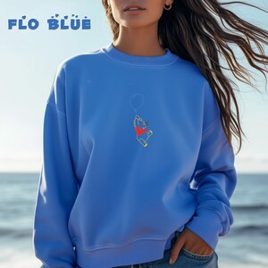 May include: A blue sweatshirt with a Winnie the Pooh graphic. The graphic shows Winnie the Pooh holding a balloon and flying through the air. The text "FLO BLUE" is printed on the top of the sweatshirt.