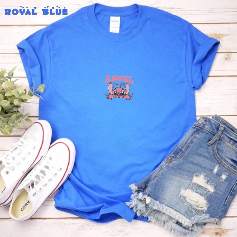 Pode incluir: Camiseta azul royal com um personagem de desenho animado rosa e a palavra "ANGEL" em rosa. A camiseta &eacute; combinada com shorts jeans e t&ecirc;nis brancos.