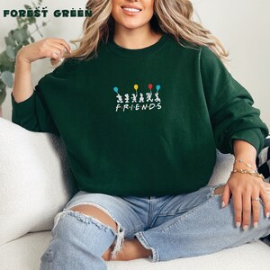 May include: A forest green sweatshirt with a graphic of six cartoon figures holding balloons and the word "FRIENDS" printed below.