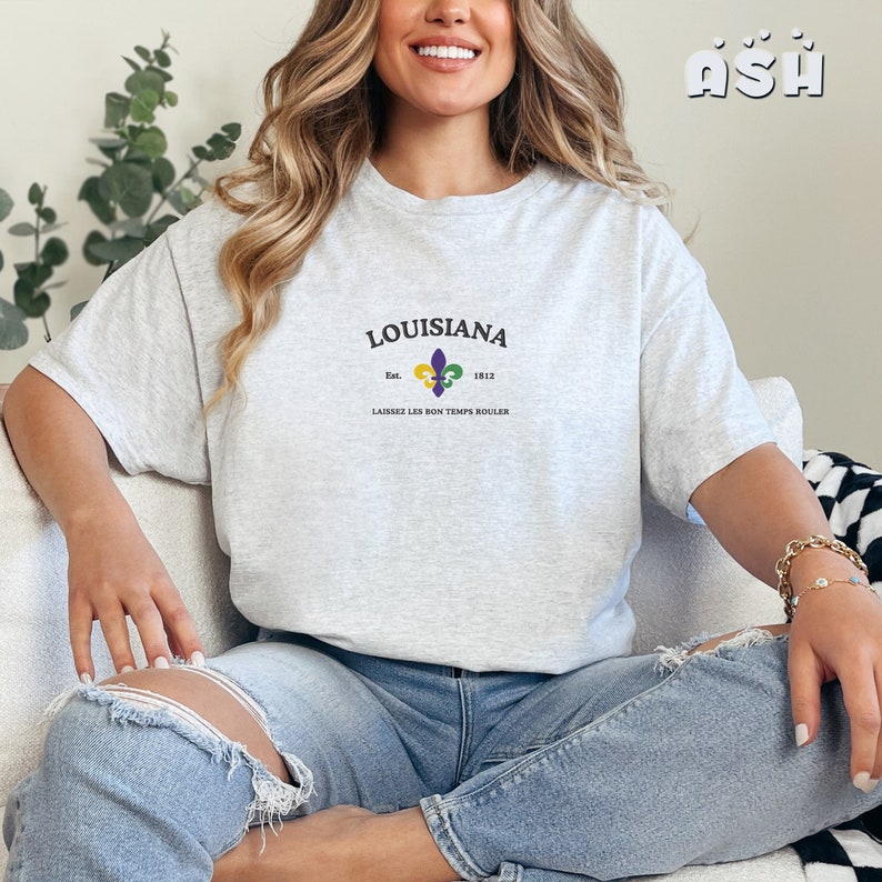 May include: A light gray t-shirt with a graphic print of a fleur-de-lis and the text "Louisiana Est. 1812 Laissez Les Bon Temps Rouler".