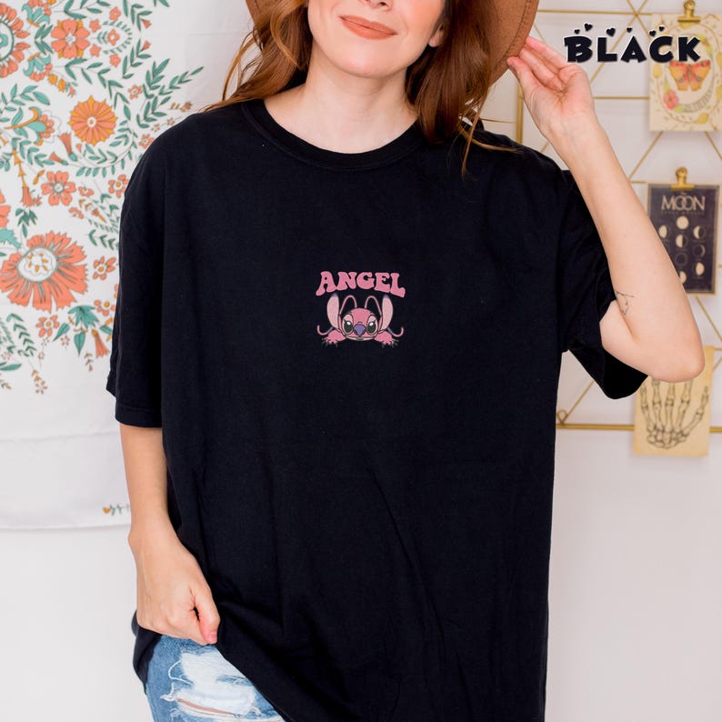 Puede incluir: Camiseta negra con un gr&aacute;fico rosa de un personaje de dibujos animados y la palabra "ANGEL" encima. La palabra "BLACK" est&aacute; impresa en blanco en la esquina superior derecha. La camiseta la lleva una persona.