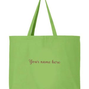 May include: A light green tote bag with long handles. The bag has the text "Your name here" in a cursive font. The bag is made of a solid color fabric and is designed for carrying items.