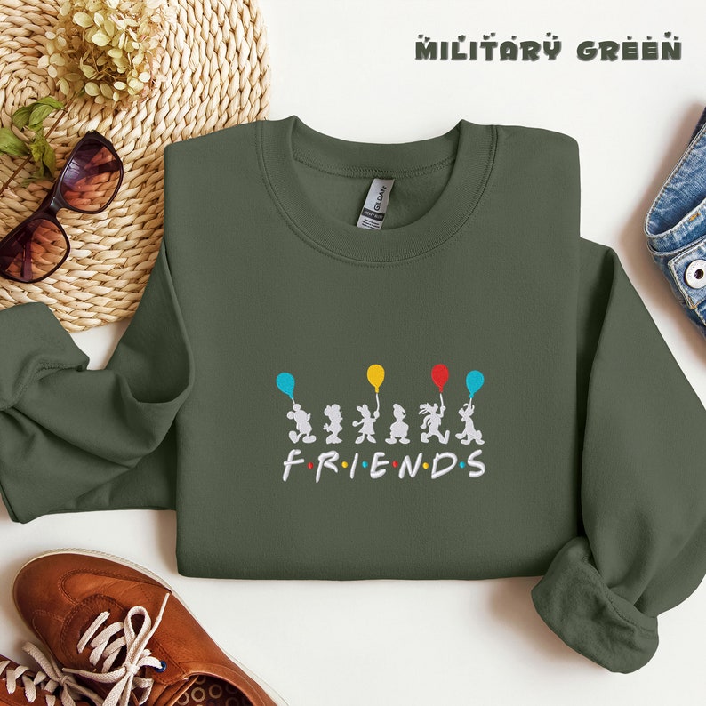 May include: A military green sweatshirt with a white graphic of six cartoon figures holding balloons and the word "FRIENDS" underneath.