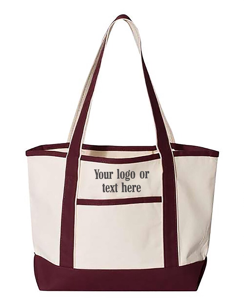 May include: Cream-coloured tote bag with burgundy accents. Features a burgundy base, trim, and handles. A front pocket is outlined in burgundy. The text "Your logo or text here" is printed on the front of the bag.
