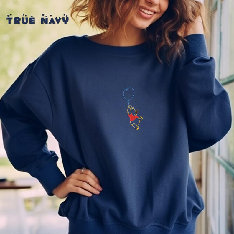 May include: A navy blue sweatshirt with a Winnie the Pooh graphic. Pooh is holding a blue balloon and is flying in the air. The text "TRUE NAVY" is printed on the top left corner of the sweatshirt.