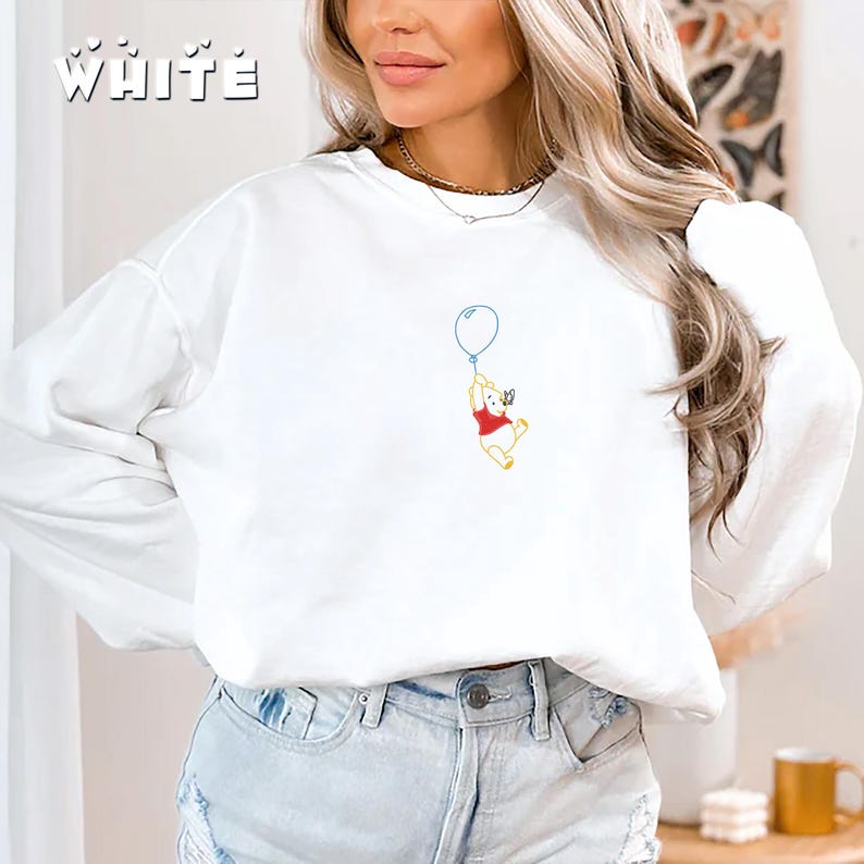May include: White long-sleeved t-shirt with a Winnie the Pooh graphic. Pooh is holding a blue balloon and flying with a butterfly.