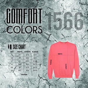 Pode incluir: Uma camisola de cor coral com uma tabela de tamanhos e as palavras "COMFORT COLORS" e "1566" em uma fonte desgastada. A tabela de tamanhos mostra as medidas em polegadas para largura, comprimento e comprimento da manga.