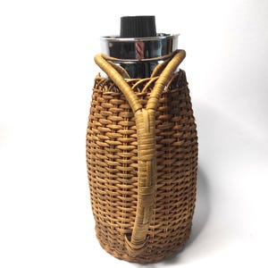 以下が含まれることがあります： 銀色の蓋と黒いトップが付いた、茶色の籐で覆われたサーマルカラフェ