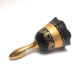 Puede incluir: Una campana de porcelana negra y dorada con un patrón floral decorativo. La campana tiene un borde festoneado y un asa dorada.