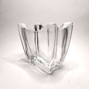 Op de afbeelding: Een heldere glazen vaas met een unieke, geschulpte rand en een vierkante basis. De vaas heeft een geometrisch ontwerp met verticale lijnen en een uitlopende vorm, geschikt voor het tentoonstellen van bloemen of decoratieve items.