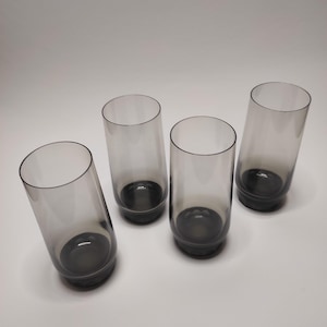 Könnte beinhalten: Vier klare Glasbecher mit einem dunkelgrauen Farbton. Die Gläser haben einen abgerundeten Boden und gerade Seiten.