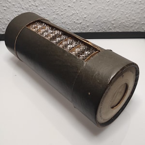 Könnte beinhalten: Eine braune Pappröhre mit einem weißen Etikett, auf dem "REGD. TRADE MARK" und "MADE IN ENGLAND" steht. Die Röhre ist mit durchsichtigen Glasperlen gefüllt.