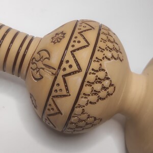 Può includere: Un vaso a forma di zucca color beige con intricati disegni marroni incisi. Il vaso presenta un lungo collo con strisce marroni verticali e un corpo bulboso adornato con motivi geometrici e floreali.