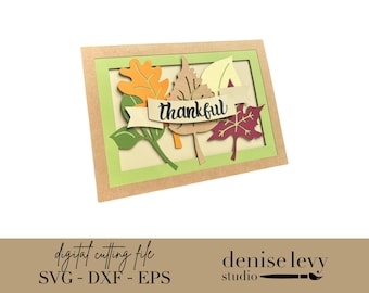 Pode incluir: Um cartão retangular com uma moldura castanha e uma borda interna verde. No interior, folhas de papel coloridas em laranja, verde e bordô são dispostas com uma faixa que diz "thankful". O cartão é um arquivo de corte digital.