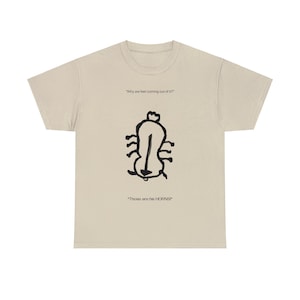 May include: A beige t-shirt with a black and white illustration of a creature with the text "Why are feet coming out of it?" and "Those are his HORNS!"