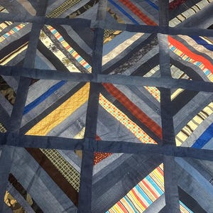 May include: A blue and white quilt made from strips of denim fabric. The quilt is made in a patchwork style with diagonal stripes.