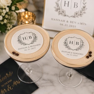 May include: Two espresso martinis with custom toppers featuring the initials "HB" and the date "06.21.2025". The drinks are garnished with coffee beans and sit on a marble surface. A sign with the same design is in the background.
