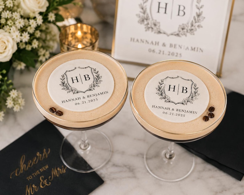 May include: Two espresso martinis with custom toppers featuring the initials "HB" and the date "06.21.2025". The drinks are garnished with coffee beans and sit on a marble surface. A sign with the same design is in the background.