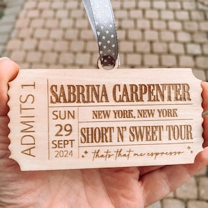 May include: A wooden ticket-shaped ornament with the text "ADMITS 1" on the left side and "SABRINA CARPENTER" on the right side. The ornament also includes the text "SUN 29 SEPT 2024", "NEW YORK, NEW YORK", "SHORT N' SWEET TOUR", and "thats that me espresso."